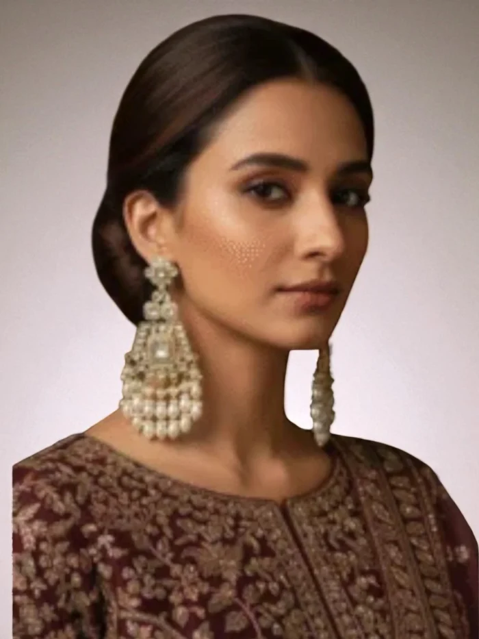 Large, elaborate white and pearl chandelier earrings worn by a woman in a maroon embroidered dress.