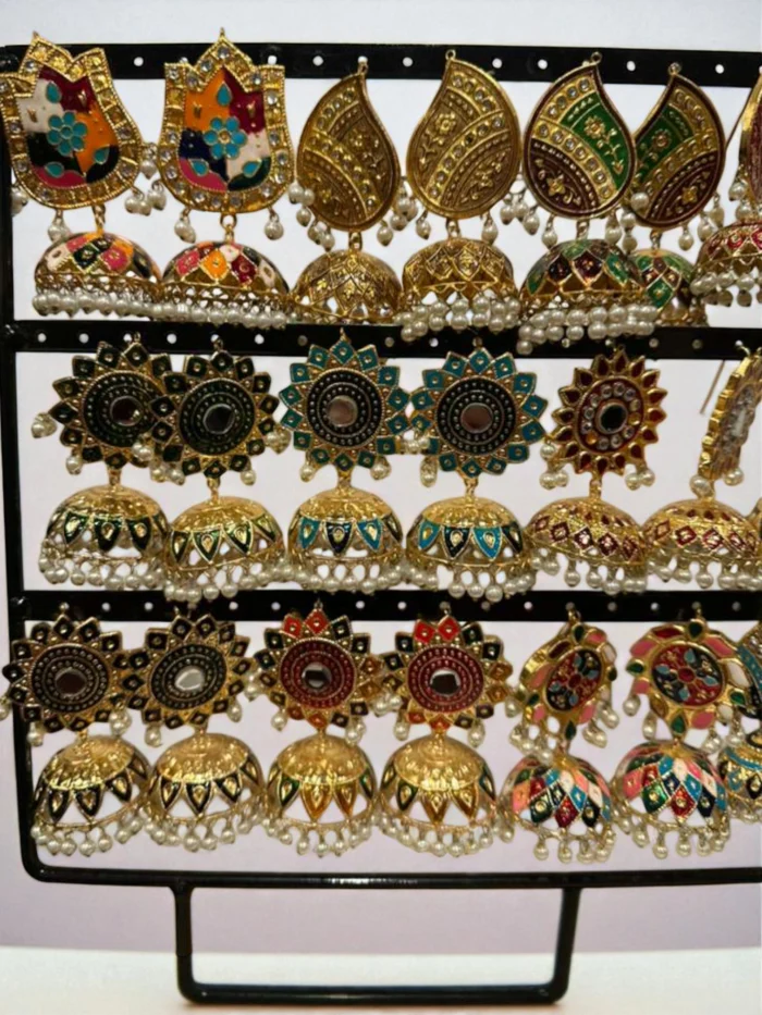 Display of numerous pairs of antique gold traditional jhumka earrings featuring intricate multi-color Meenakari enamel painting and small pearl drops.