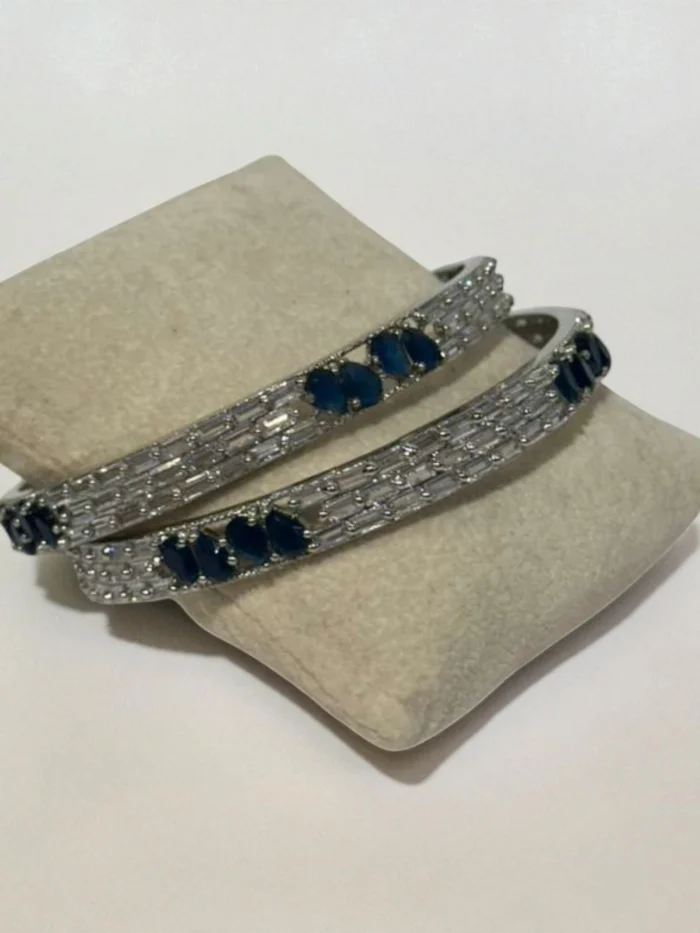 Pair of silver plated bangles set with alternating clear baguette crystals and marquise-cut sapphire blue stones.