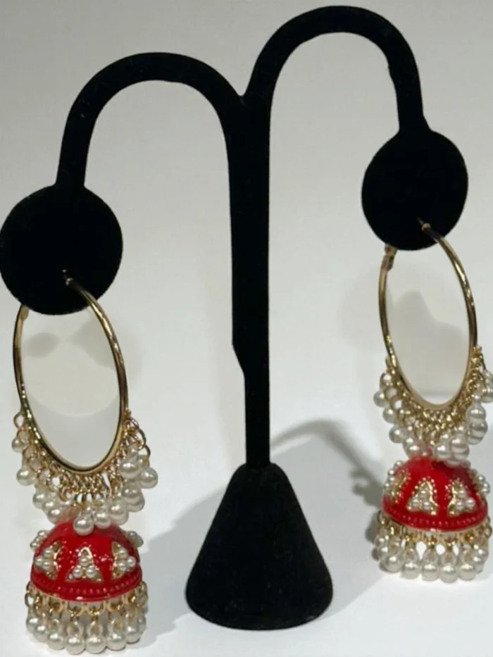 Pair of red enamel gold-plated Bali Jhumki earrings with white faux pearl drops displayed on a black earring stand.
