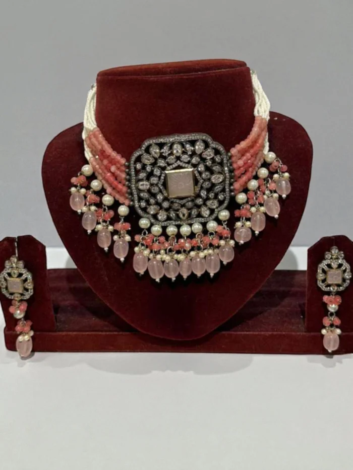 Pink Pachhi Kundan choker necklace set with antique finish metal and pink onyx beaded drops displayed on a reddish-brown velvet jewelry bust.