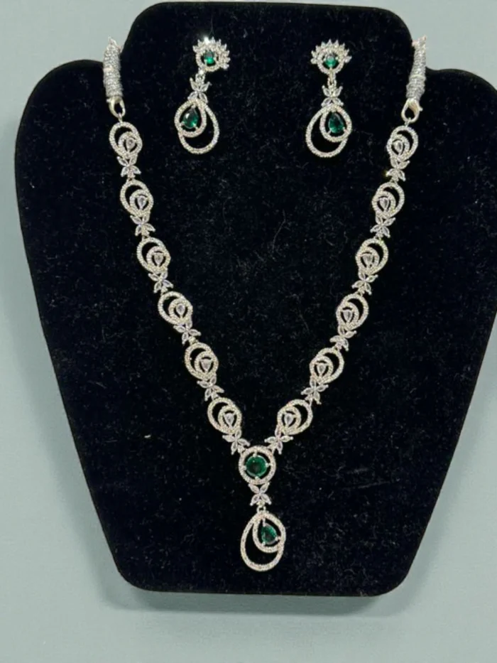 American Diamond necklace and earring set in silver polish, featuring a linked design with central green and mint colored stones, displayed on a black jewelry bust.