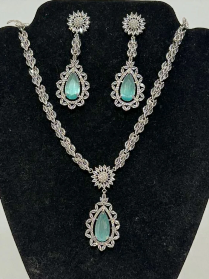 American Diamond necklace and earring set in silver polish with a large mint/aqua teardrop central stone, displayed on a black jewelry bust.