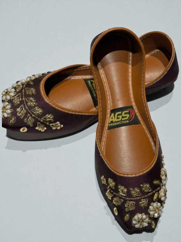 Pair of deep purple Punjabi Jutti flats with gold zari thread and white bead floral embroidery, featuring a tan leather inner sole and a 'AGS Production' label.