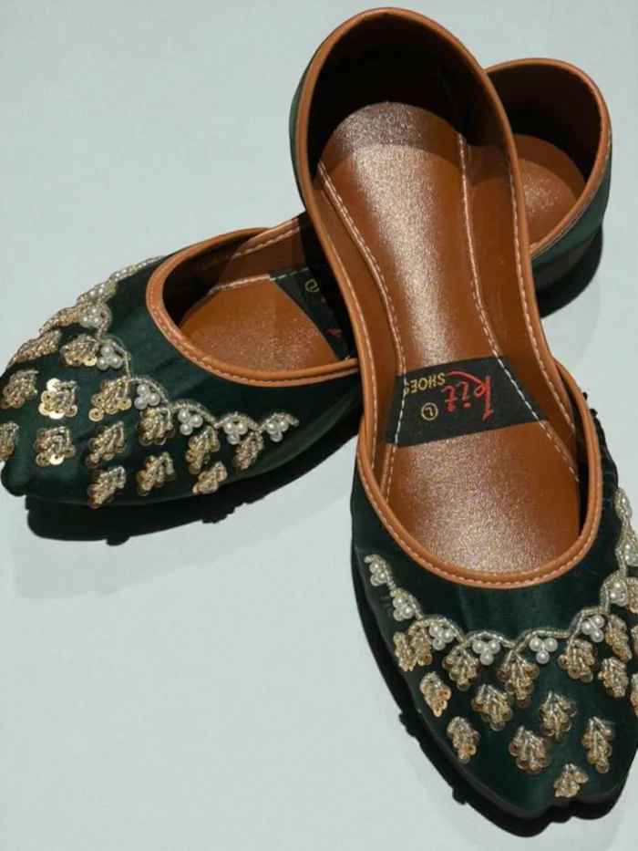 Pair of deep emerald green Punjabi Jutti flats with gold zari thread, sequin, and pearl hand work in leaf motifs, featuring a tan leather inner sole with a 'Kit Shoes' label.