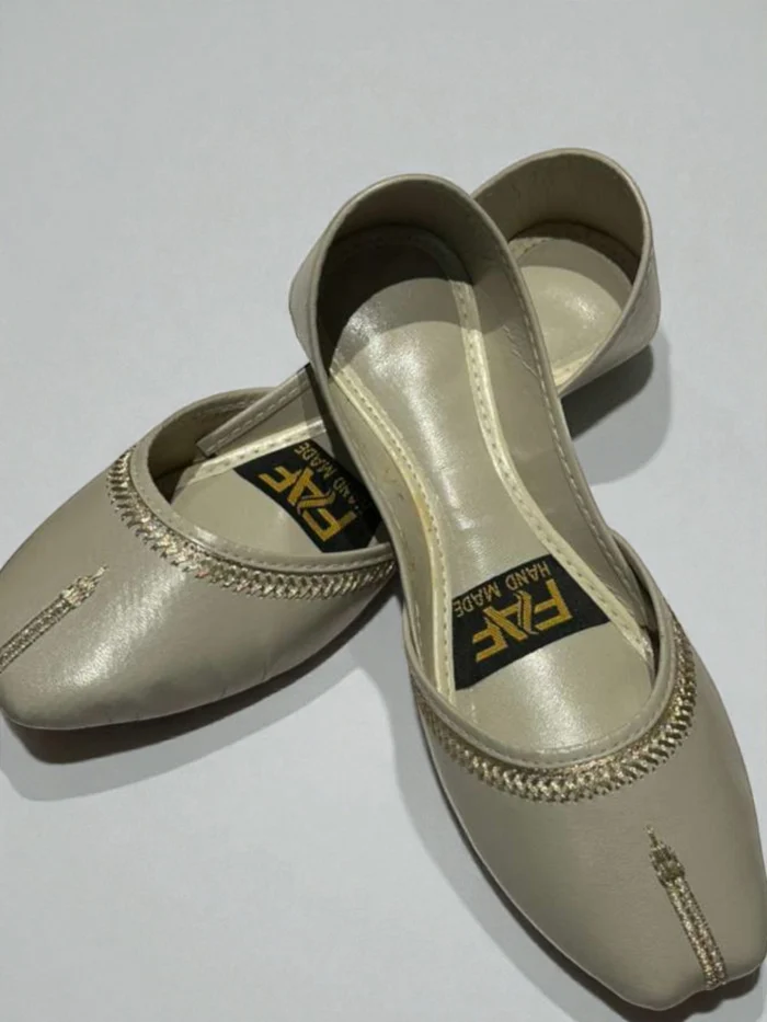 Pair of plain grey leather Punjabi Jutti flats with subtle gold thread hand stitching on the collar and toe, featuring a tan leather inner sole with a 'HAND MADE' label.