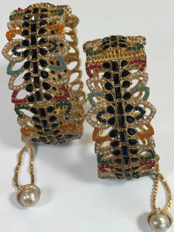 Pair of broad, openable gold plated kada bangles featuring intricate multi-colored Nauratan stones, central black stones, and a hanging pearl drop.