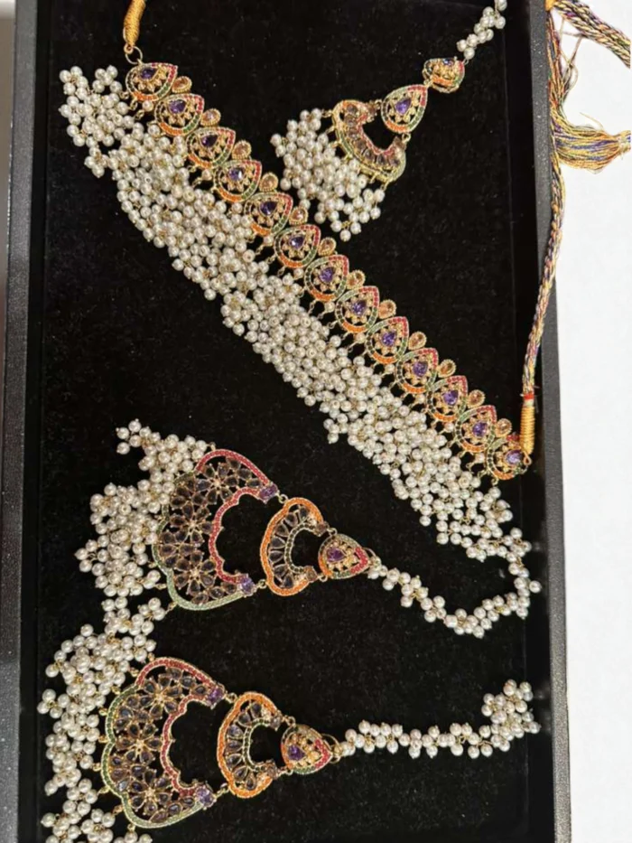 Gold plated Nauratan choker set featuring purple accent stones, multi-color enamel work, and heavy faux pearl drops. Set includes choker, oversized earrings, and a maang tika, displayed in a box.