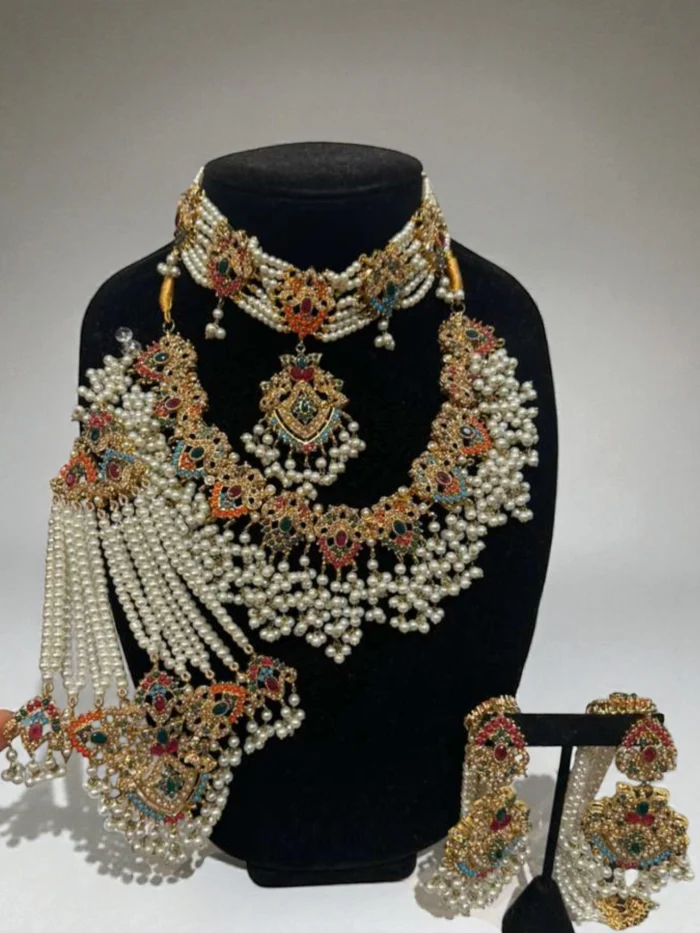 Complete gold plated Nauratan bridal jewelry set featuring multi-color stones and heavy white faux pearl tassel drops. The set includes a choker, long necklace, earrings, maang tika, and a jhumar.