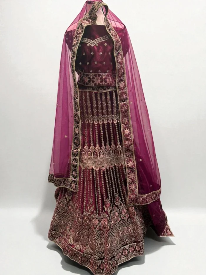 Mannequin wearing a deep plum velvet bridal lehenga set with heavy gold zari and stone embroidery, styled with a matching net dupatta draped over the head.