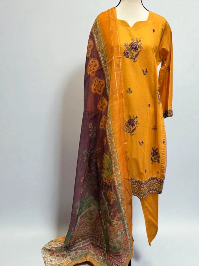 Mannequin wearing a mustard yellow cotton Kurta with purple and green floral embroidery and printed borders, matching trousers, and a purple, yellow, and orange Doria printed dupatta.