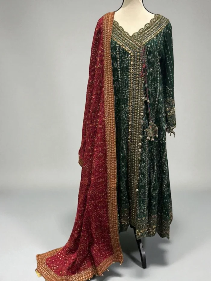 Mannequin wearing a long, full-sleeved emerald green Shafoon Angrakha dress with heavy gold sequins and pearl embroidery, styled with a contrasting red heavy embroidered shawl.
