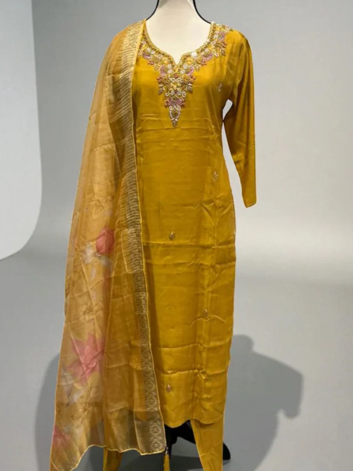 Mannequin wearing a mustard yellow muslin Kurta with a heavily hand-embroidered neckline in pink, gold, and white, paired with matching trousers and a sheer patterned dupatta.