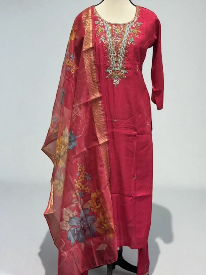 Mannequin wearing a hot pink muslin Kurta with a heavily hand-embroidered neckline featuring mirrors, beads, and colorful threadwork, paired with a matching bottom and a sheer floral printed dupatta with a gold border.