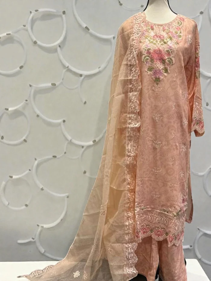 Mannequin wearing a peach Karandi suit with pink and green floral thread embroidery, self-print trousers, and a sheer peach Khadi net dupatta with a scalloped embroidered border.